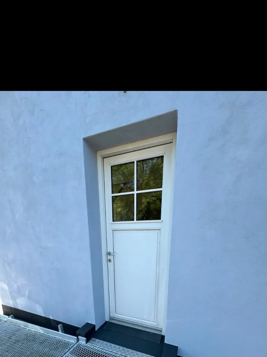 Nymalet hvid yderdør med mørk sokkel og ren kant mod pudset mur