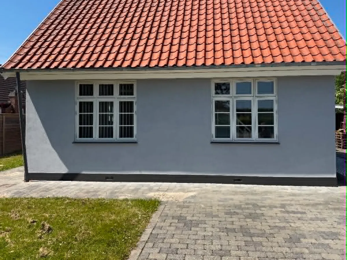 Samme hus efter facademaling, lys puds, mørk sokkel og nymalede vinduer